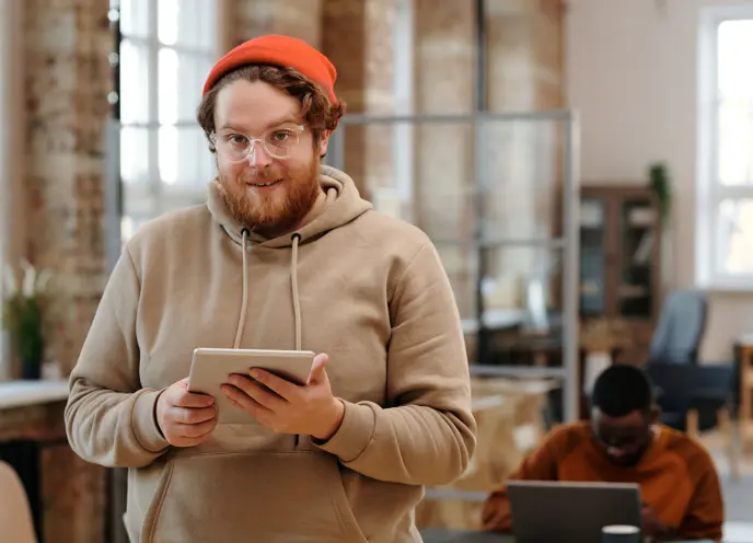 Smilende mann med iPad i et moderne kontormiljø, som jobber effektivt og produktivt